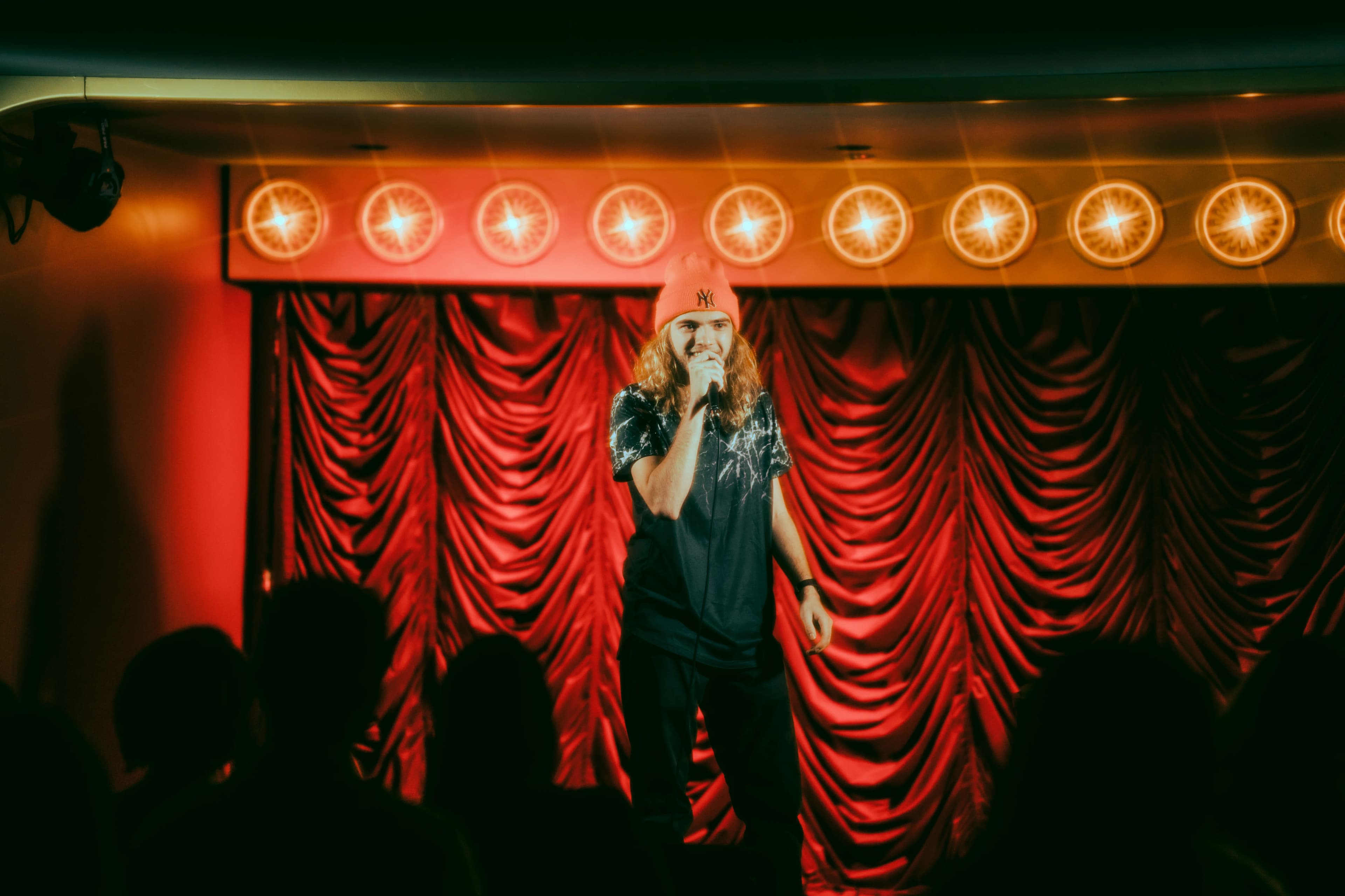 A comedian at the mic in front of the red curtain
