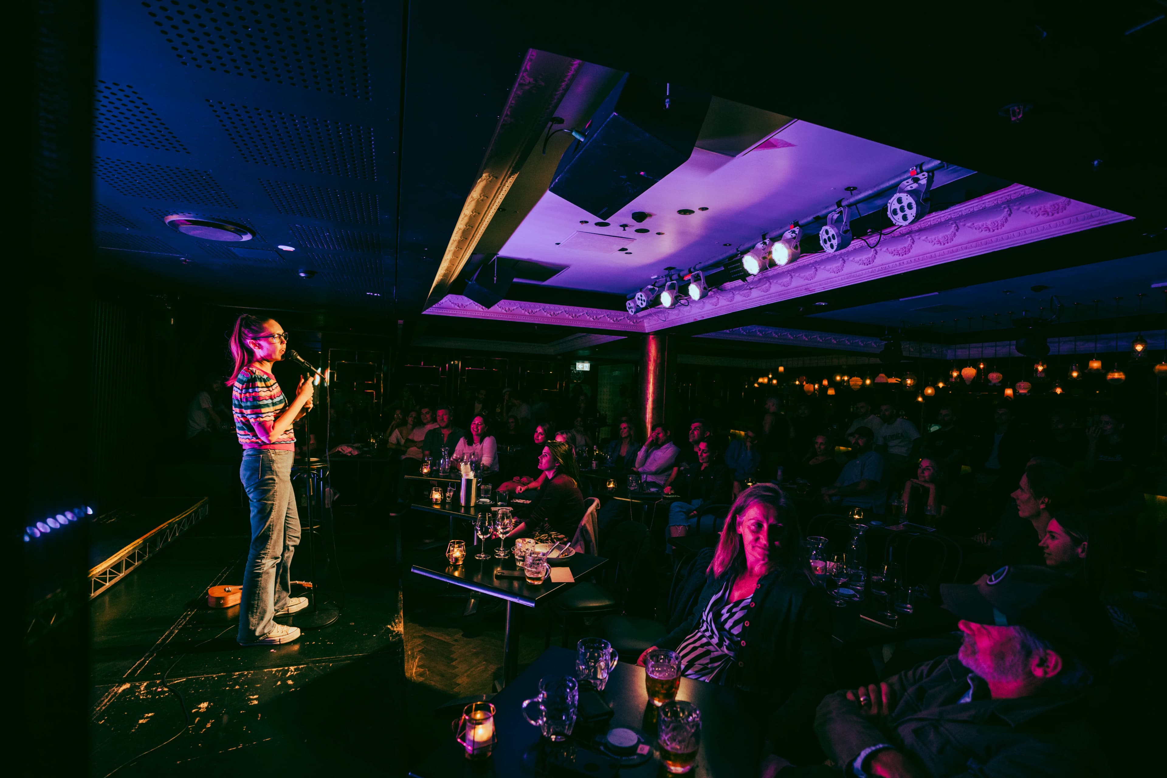 Host Stephanie Broadbridge on stage at the venue, crowd at candle-lit tables